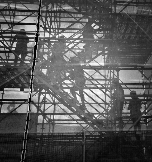 a black and white image of construction workers scaling scaffolding